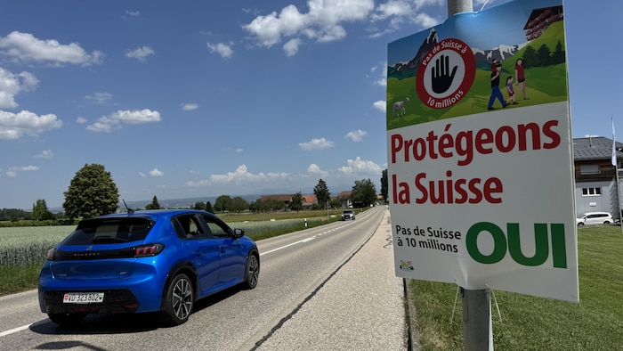 Une voiture circulant sur une route passe à côté d'une pancarte où l'on peut lire « Protégeons la Suisse, Oui ».