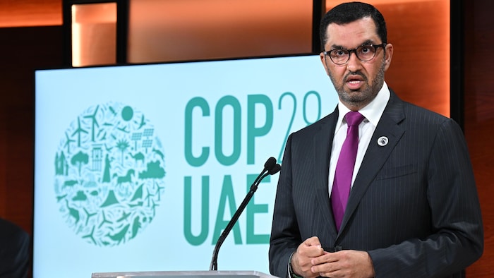Le président de la COP28, Sultan Ahmed Al-Jaber, devant un panneau avec un dessin et des inscriptions indiquant COP28 UAE.