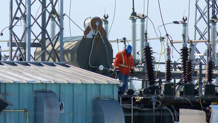 Un travailleur marche au milieu d'équipement électrique en plein air.
