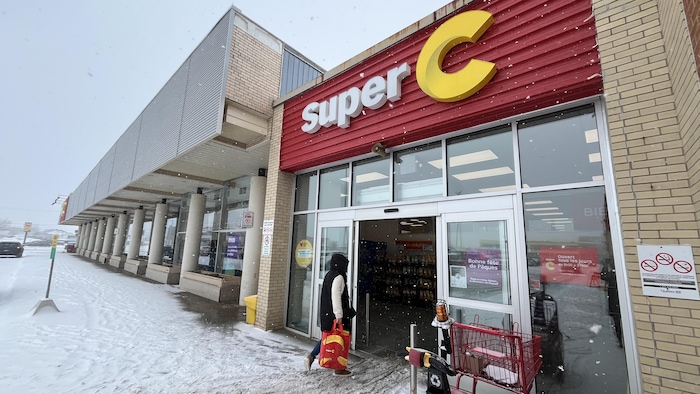 Une personne portant des sacs de courses entre dans une épicerie Super C sous la neige.