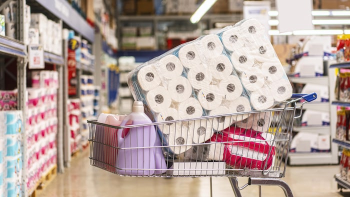 Un panier rempli de produits, notamment de rouleaux de papier toilette, dans un supermarché.