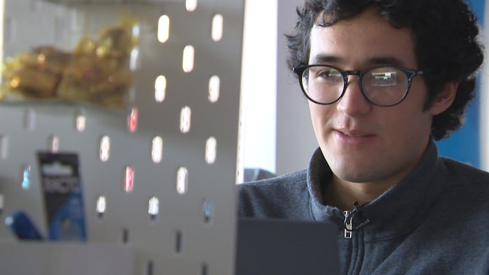 Un homme portant des lunettes sourit, assis à un bureau.