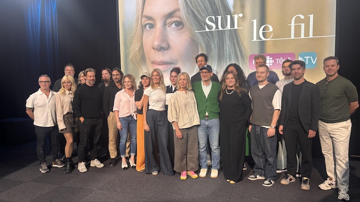 Les acteurs et les producteurs posent devant une affiche de la série.
