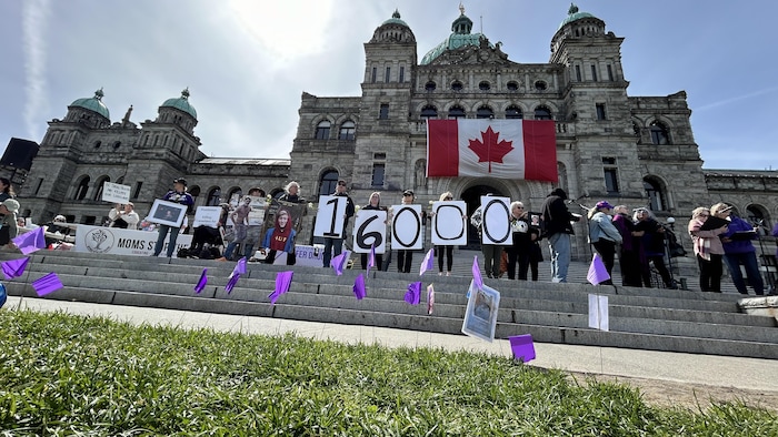 Un groupe de gens se tiennent sur les marches du parlement de Victoria, tenant des pancartes avec les chiffres 1 6 0 0 0.