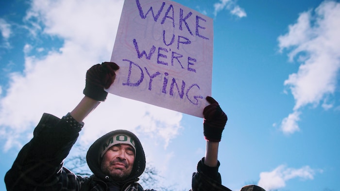 Un homme tient une affiche sur laquelle on lit: «Réveillez-vous, nous mourrons», en anglais.