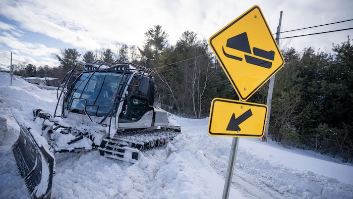 Une machine en train de circuler sur un amoncellement de neige avec un panneau qui présente un sentier de motoneige.