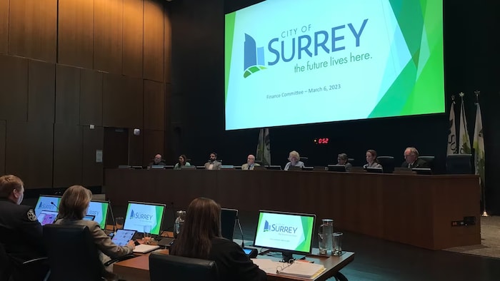 Les membres du conseil municipal de Surrey en discussion dans une salle, sous un grand écran sur lequel est projeté un document. 