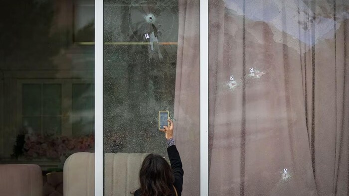 Une femme prend des photos des impacts de balles sur les fenêtres d'une entreprise avec son cellulaire.