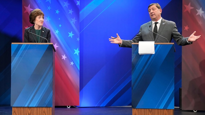 Susan Collins regarde Troy Jackson qui s'exprime les bras ouverts derrière un pupitre.