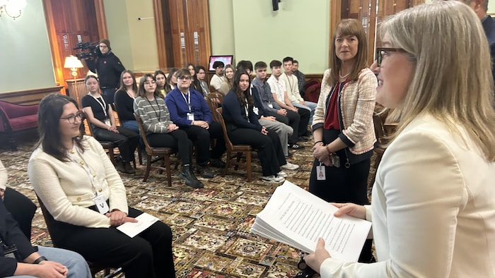 Susan Holt tiens dans ses mains une pile de lettres, elle s'adresse au groupe de jeunes à l'Assemblée Législative. 