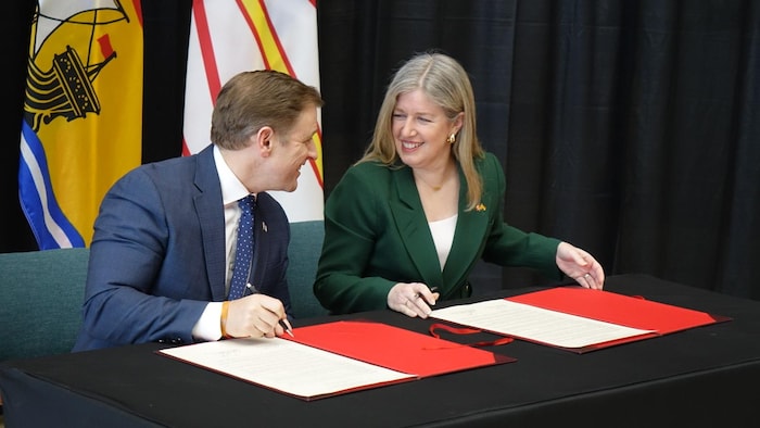 Deux personnes à une table qui signe des documents.