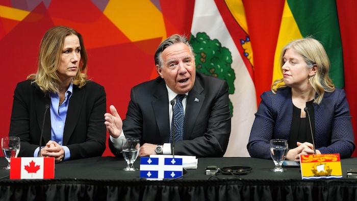 L'ambassadrice du Canada aux États-Unis la première ministre du Nouveau-Brunswick regardent le premier ministre du Québec prendre la parole pendant une conférence de presse.