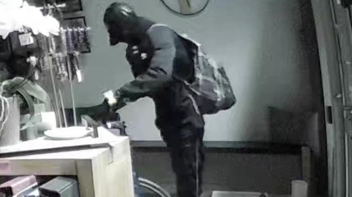 An individual dressed from head to foot holds a bicycle and is inside a business. it smashes wall broke two