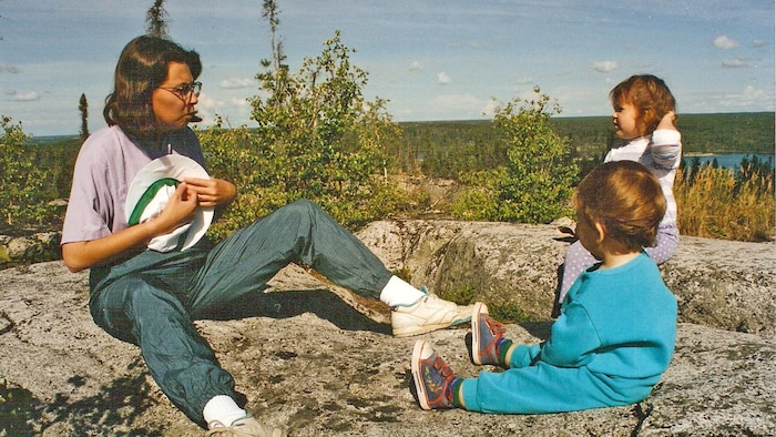 Une image datant de 1996 de Suzette Montreuil assise sur des roches avec ses deux jeunes enfants.