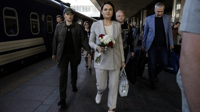 Une femme marche sous escorte en tenant un bouquet de fleurs.