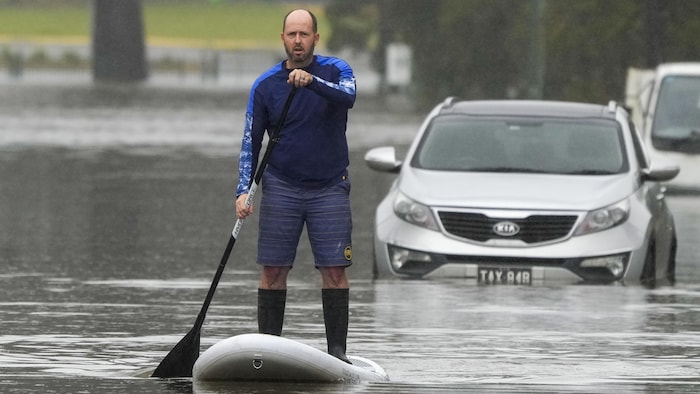 Un homme se tient debout sur une planche à pagaie au milieu d'une rue inondée.
