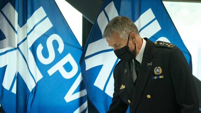 Sylvain Caron, masqué, devant des drapeaux du SPVM.