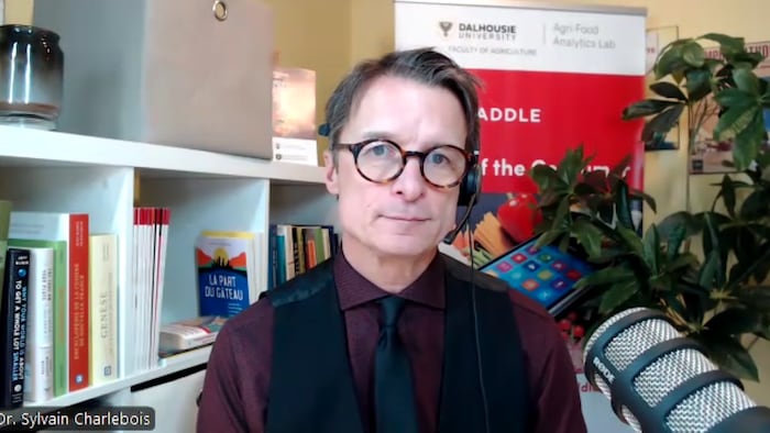 Sylvain Charlebois pose en en entrevue devant une bibliothèque et un micro.