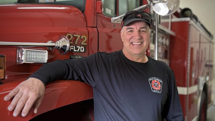 Sylvain Dugas pose devant la caméra, accoté sur un camion de pompier à l'intérieur d'une caserne.