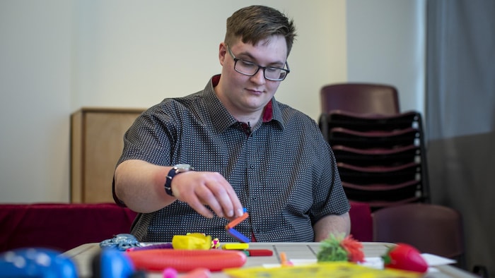 Un jeune homme plutôt corpulent jouant avec des jouets multicolores à une table.