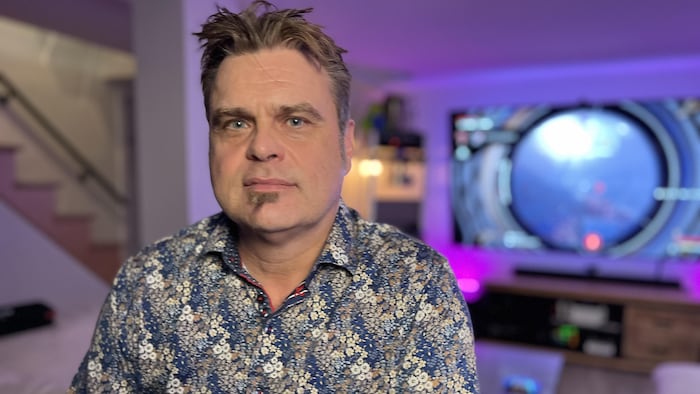 Un homme prend la pose, dans son salon, avec des néons mauve et bleu.
