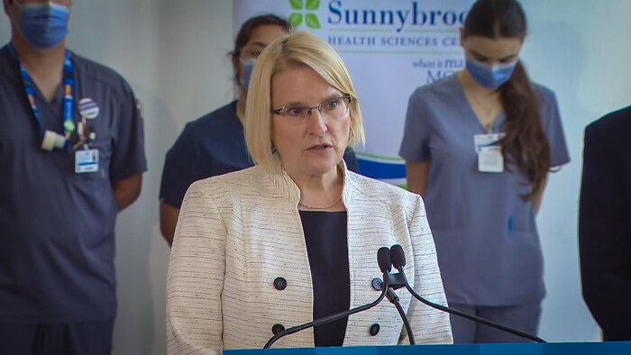 وزيرة الصحة في حكومة أونتاريو، سيلفيا جونز، تلقي كلمة في مستشفىً في تورونتو  ونرى خلفها ممرضات.