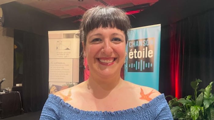 Une femme souriante devant la bannière du Gala de la chanson de Caraquet. 