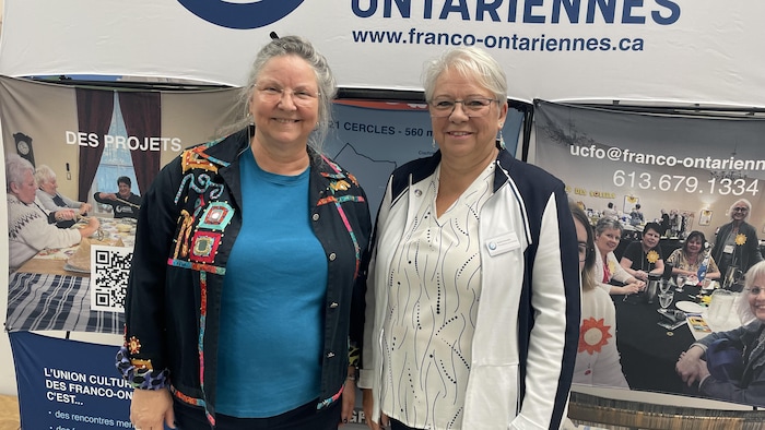Deux femmes debout devant des pancartes de l’organisme Union culturelle des Franco-Ontariennes.
