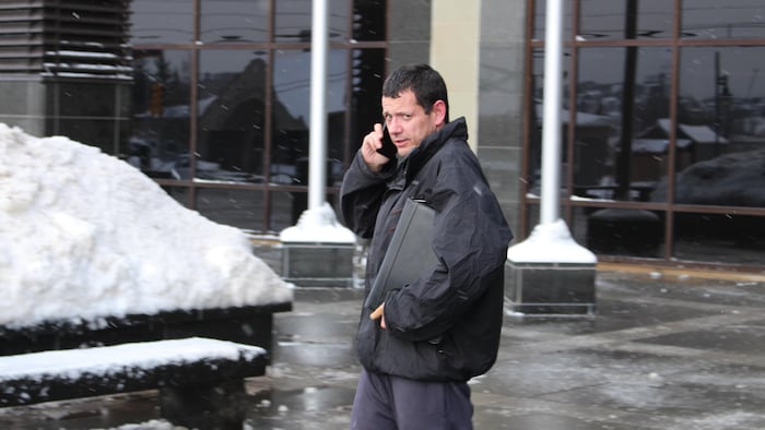 Sylvio Saunier se tient debout devant un palais de justice et parle au téléphone.