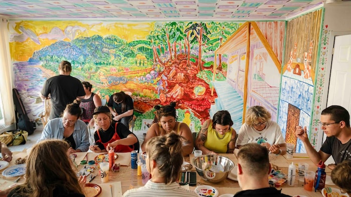 Un plan moyen capturant l'atmosphère vibrante et colorée d'une salle d'atelier d'art. Le plafond est recouvert de tuiles peintes à la main avec des motifs colorés.