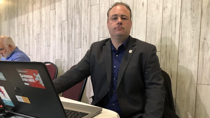 Mathieu Lavoie regarde la caméra, il est assis à une table avec un ordinateur portable. 