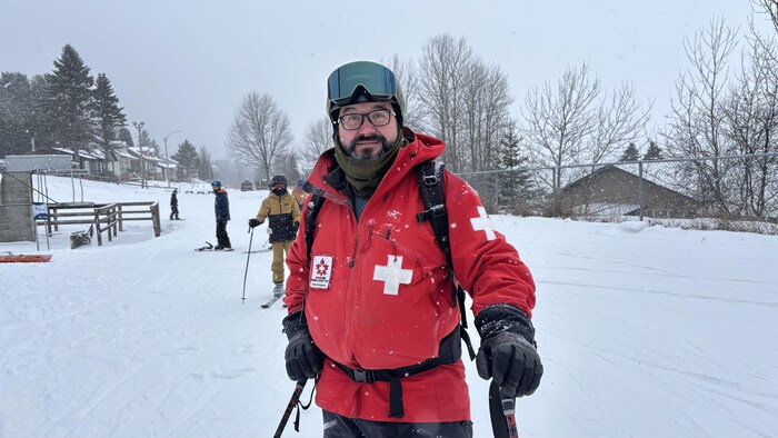Un homme en manteau rouge et en ski pose devant les pentes. 