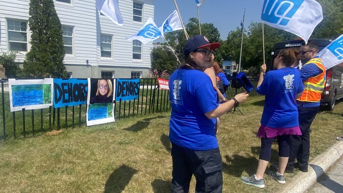 Des personnes brandissent des drapeaux devant un immeuble. Le visage de Nathalie Petitclerc est affiché sur une clôture.