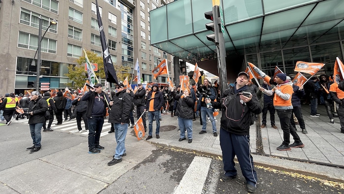 Des syndiqués manifestent devant le Palais des congrès en brandissant des drapeaux et en bloquant une rue.