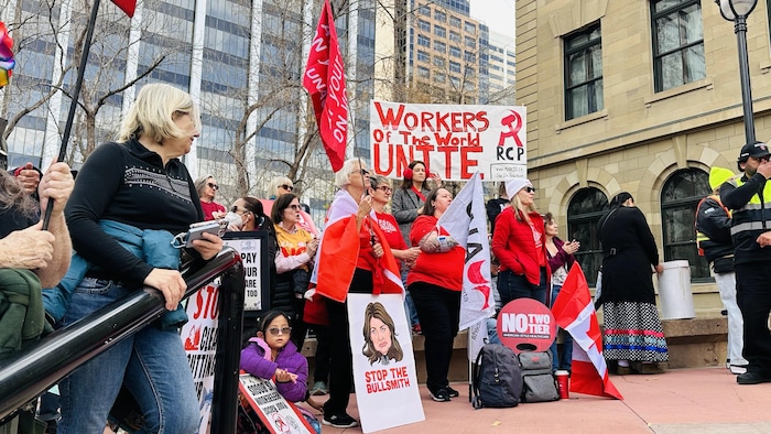 Des manifestants tiennent des pancartes avec des symboles communistes au rassemblement de la Fédération des travailleurs de l’Alberta