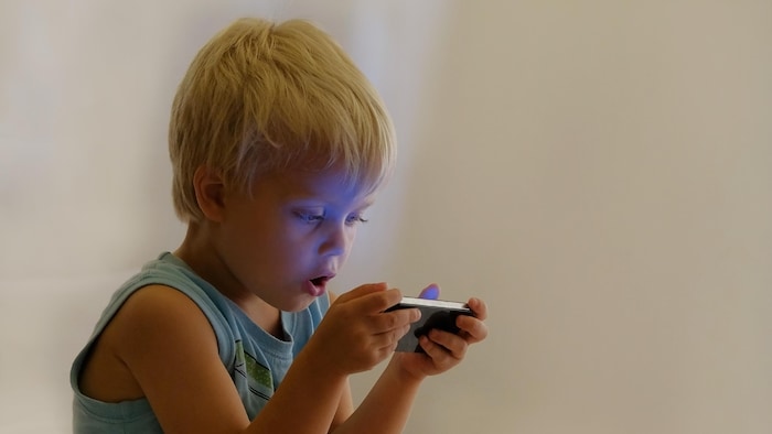 Little cute boy enthusiastically playing video games on portable device. For fun and joy. Concept: cell phone addiction