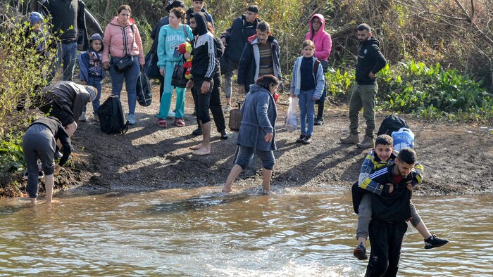 Des hommes, des femmes et des enfants traversant une rivière.
