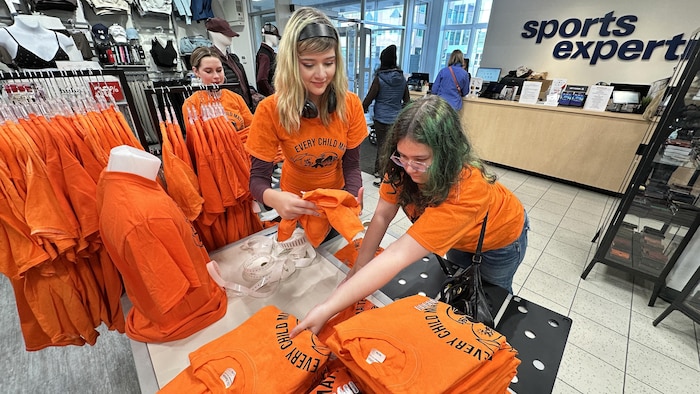 Des élèvent plient et étiquettent des chandails dans un magasin.