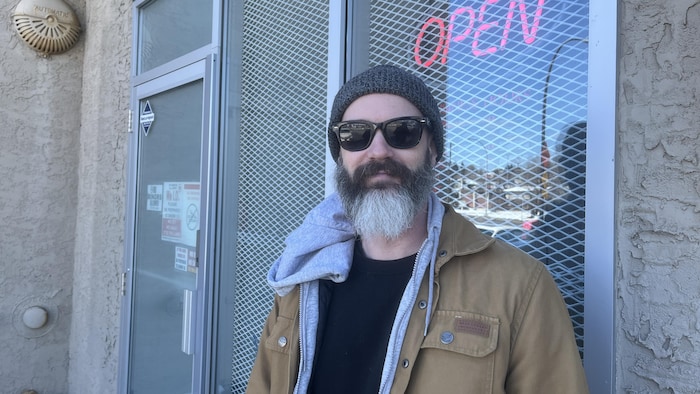Un homme est debout devant un commerce ou l'on voit une enseigne qui dit «ouvert» en anglais. 
