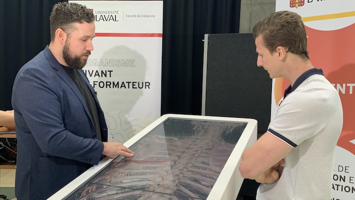 Philippe Chassé et un démonstrateur sont penchés au-dessus d'un grand écran tactile.