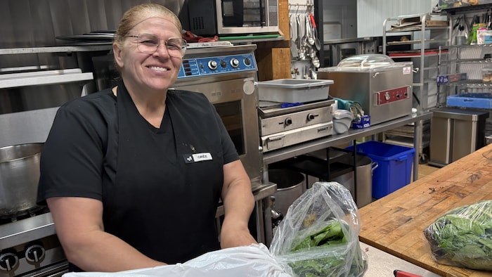 La copropriétaire sourit alors qu'elle trie des épinards dans la cuisine de son établissement.
