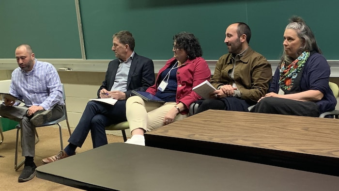 Dans une salle de cours d'une université, un homme assis sur une chaise à l'extrême gauche de la photograph est penché vers l'avant. Quatre autres personnes assises sur des chaises à sa gauche le regardent.