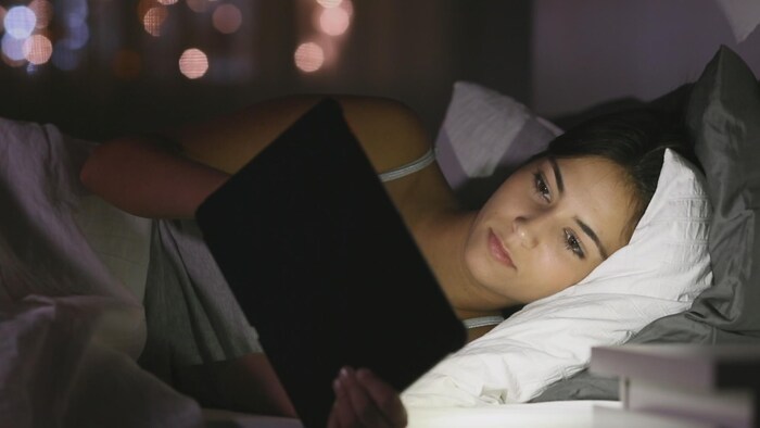 Une jeune fille couchée regarde une tablette électronique.