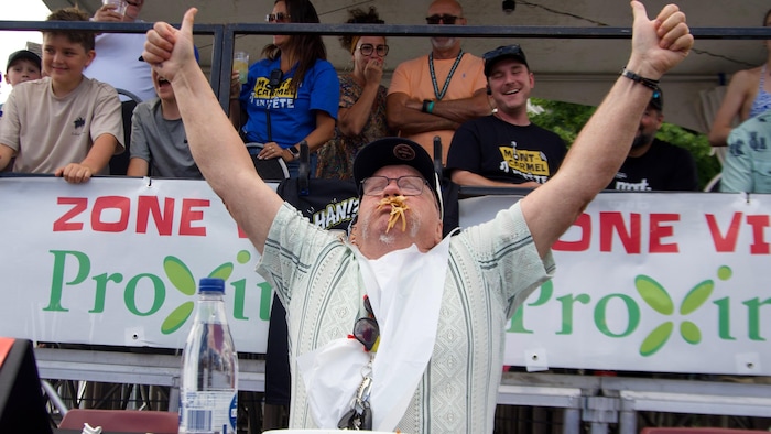 Un homme levant les bras en l'air, la bouche pleine de spaghettis. 