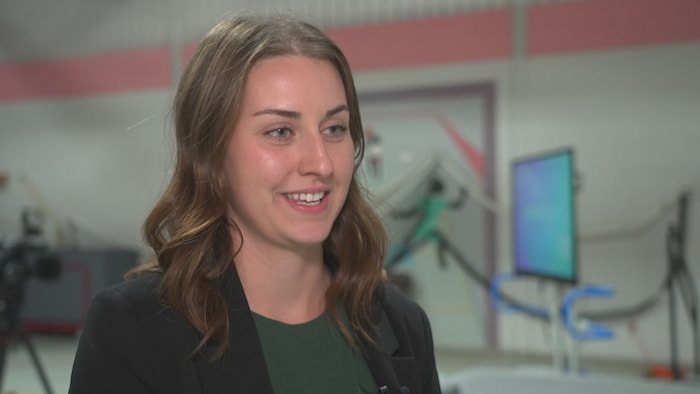 Plan rapproché de Gabrielle Pineault, souriante lors d'une entrevue. Elle a les cheveux bruns ondulés et porte un veston noir sur un haut vert.