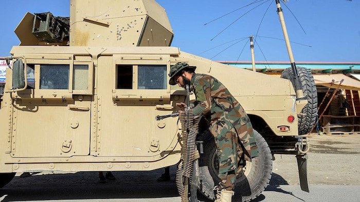 Un soldat en habit de camouflage, à côté d'un véhicule blindé, transporte une mitrailleuse et des bandes de munitions.