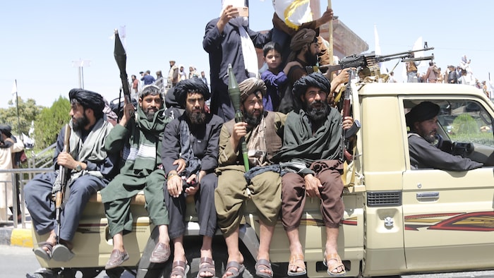 Des hommes armés portant des tuniques afghanes dans la boîte d'une camionnette.