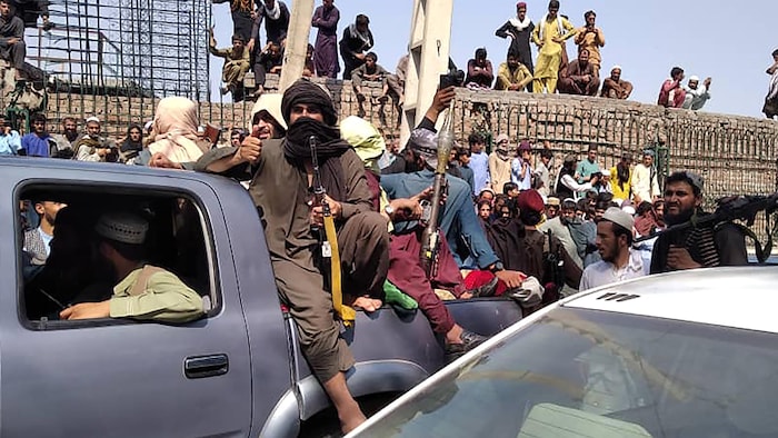 Des talibans armés dans la boîte d'une camionnette, sous le regard de nombreux résidents.