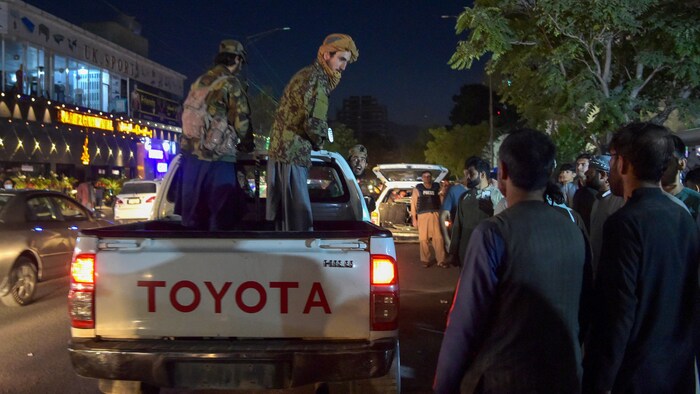 Des combattants talibans se tiennent debout sur une camionnette, alors qu'une foule s'est massée autour d'eux.