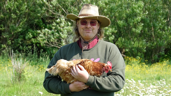 Tam Desgroseilliers photographié avec une poule dans les mains.